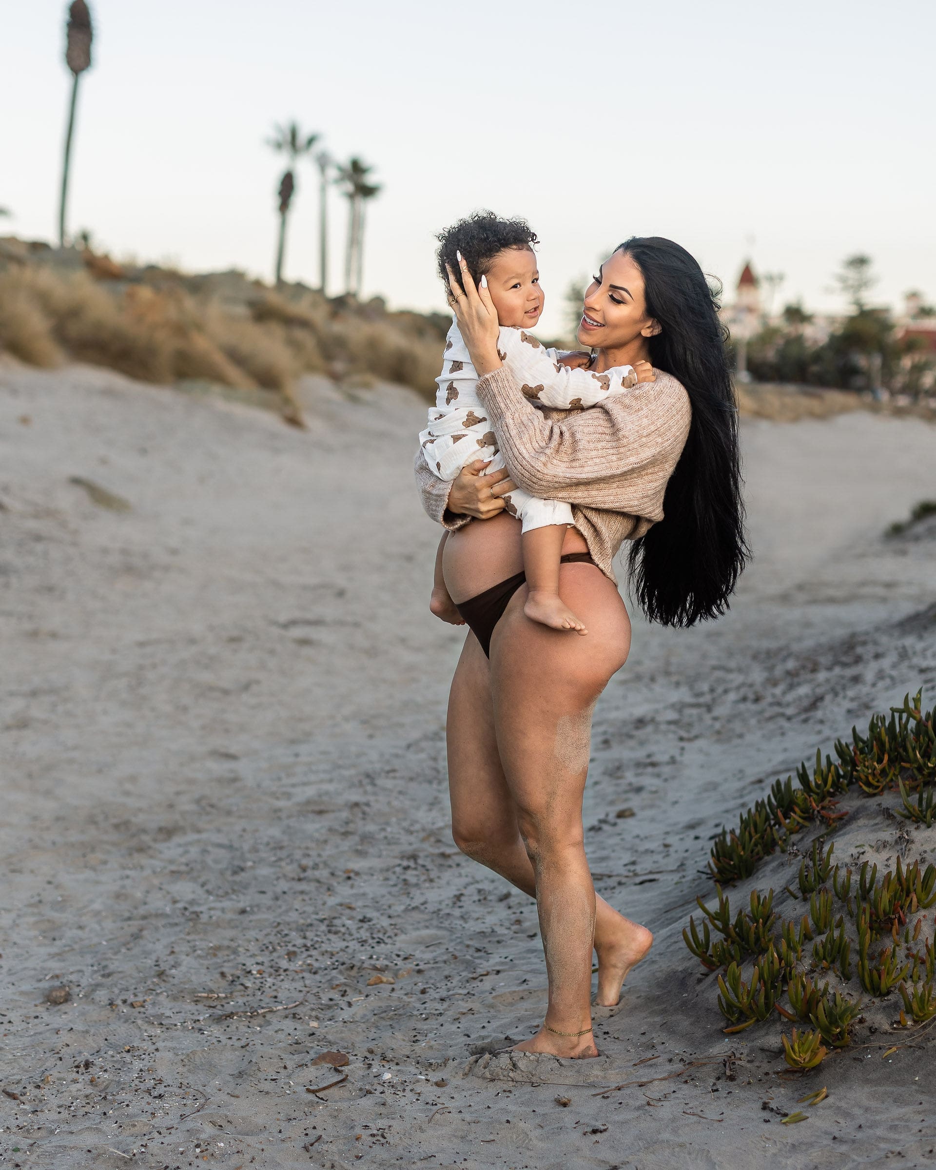 A happy expectant mother walks on a beach with her toddler sitting on her bump at sunset after visiting birth centers in san diego
