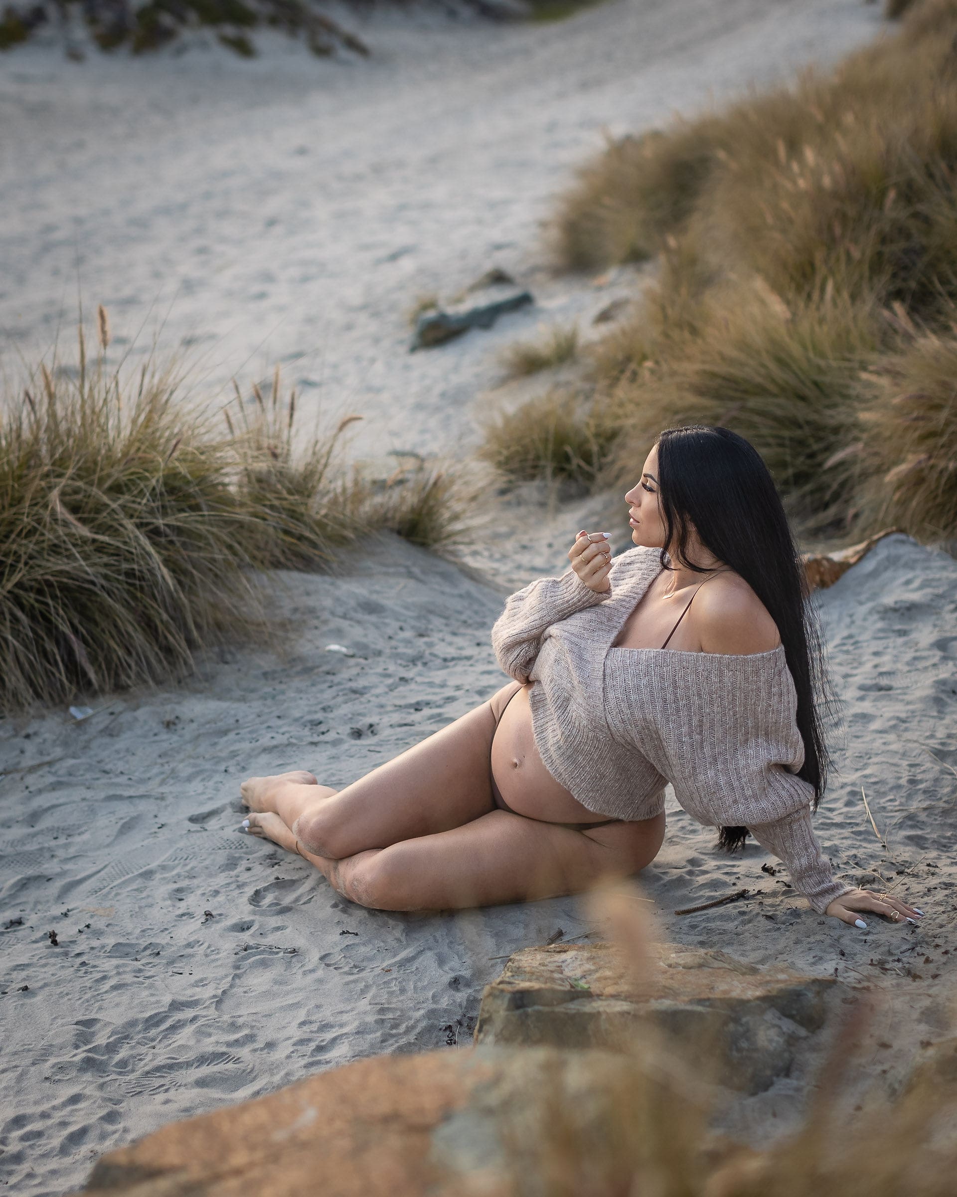 A pregnant woman lounged on a beach in a tan sweater with bump out at sunset after visiting birth centers in san diego