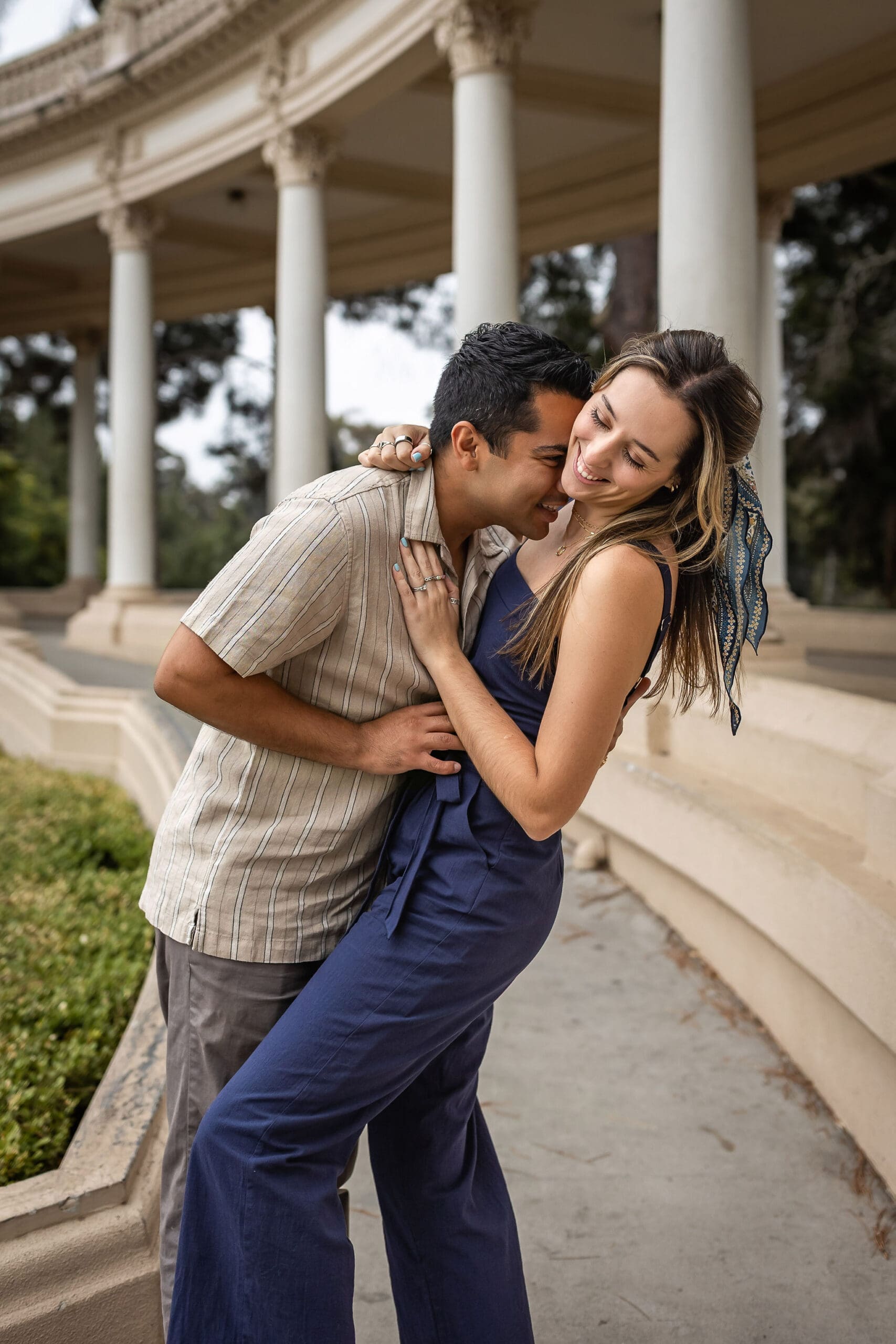 A laughing couple giggles in a garden in blue and grey