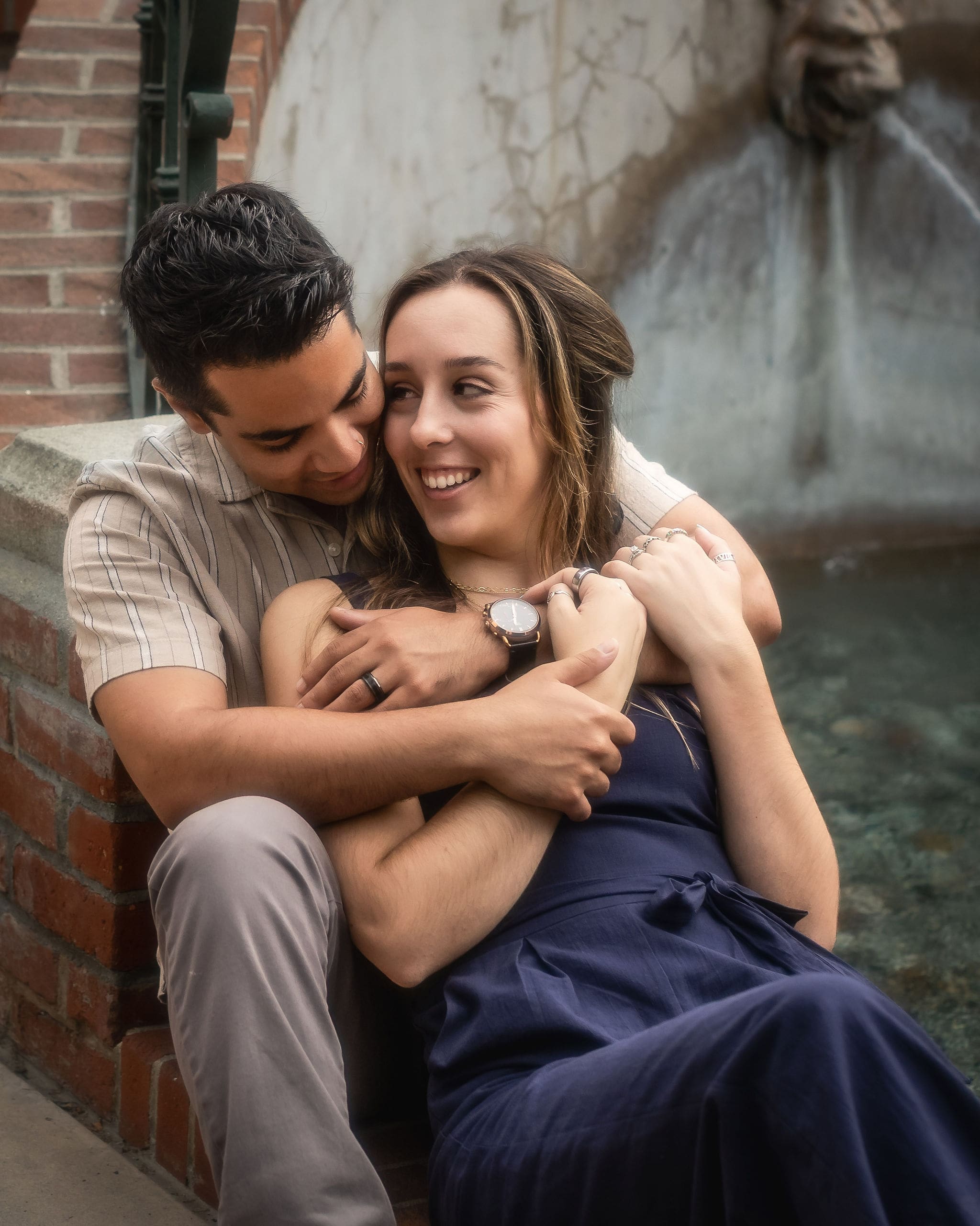 A woman in blue snuggles in the lap of her partner in tan as they both smile after a couples massage in san diego