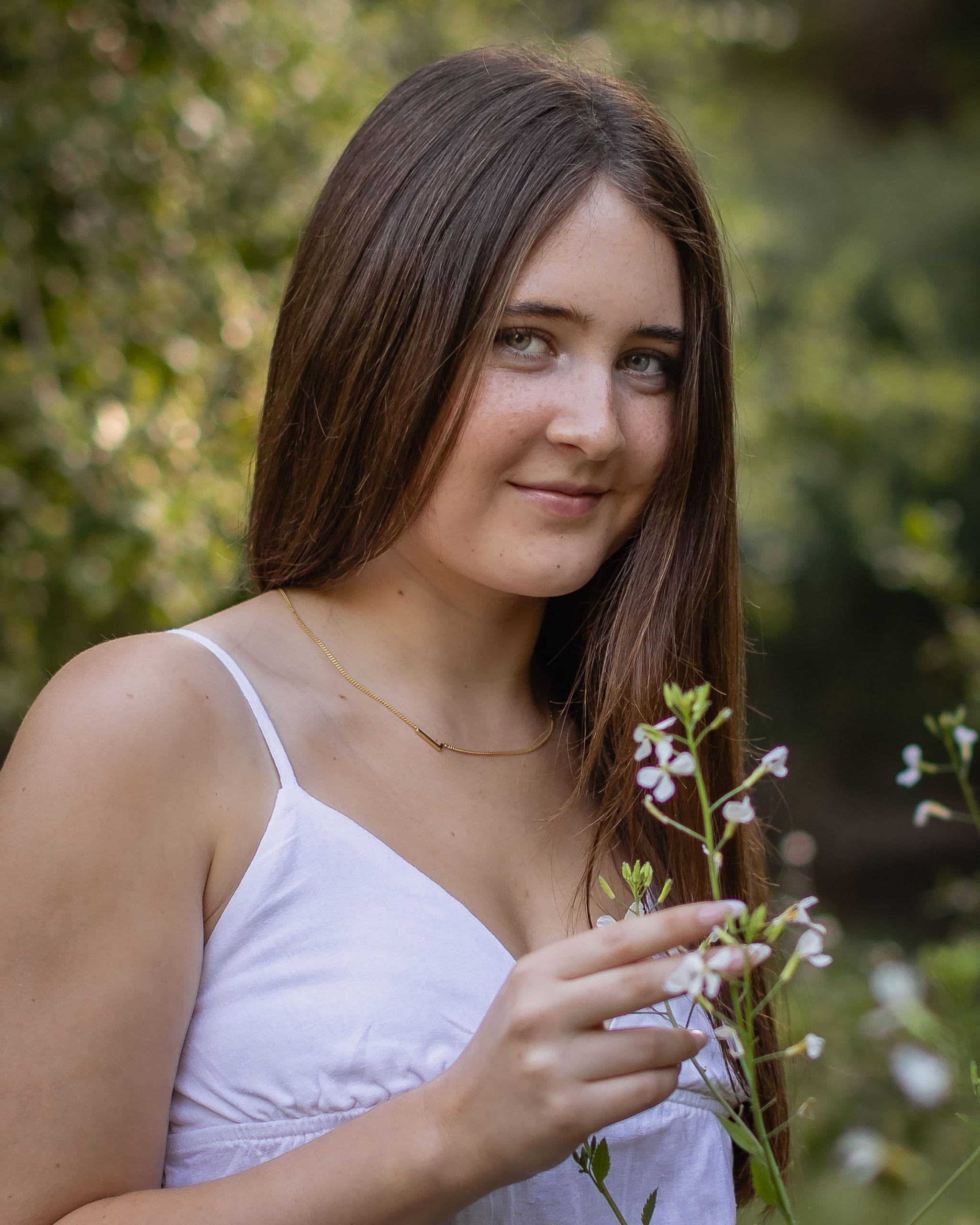A high school senior smells some small flowers while standing in a white dress in a close up after finding great nail salons in san diego