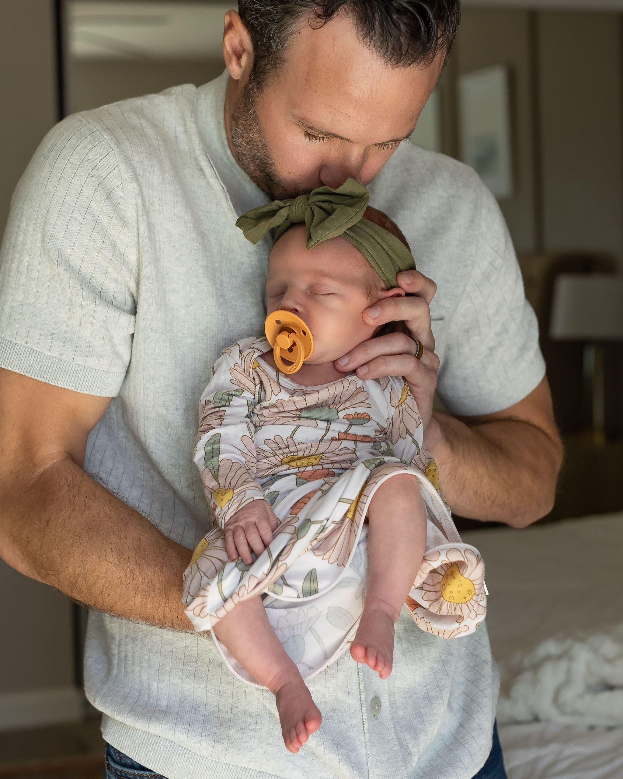 A new dad cradles his sleeping newborn daughter against his chest while kissing her head after meeting nannies in san diego