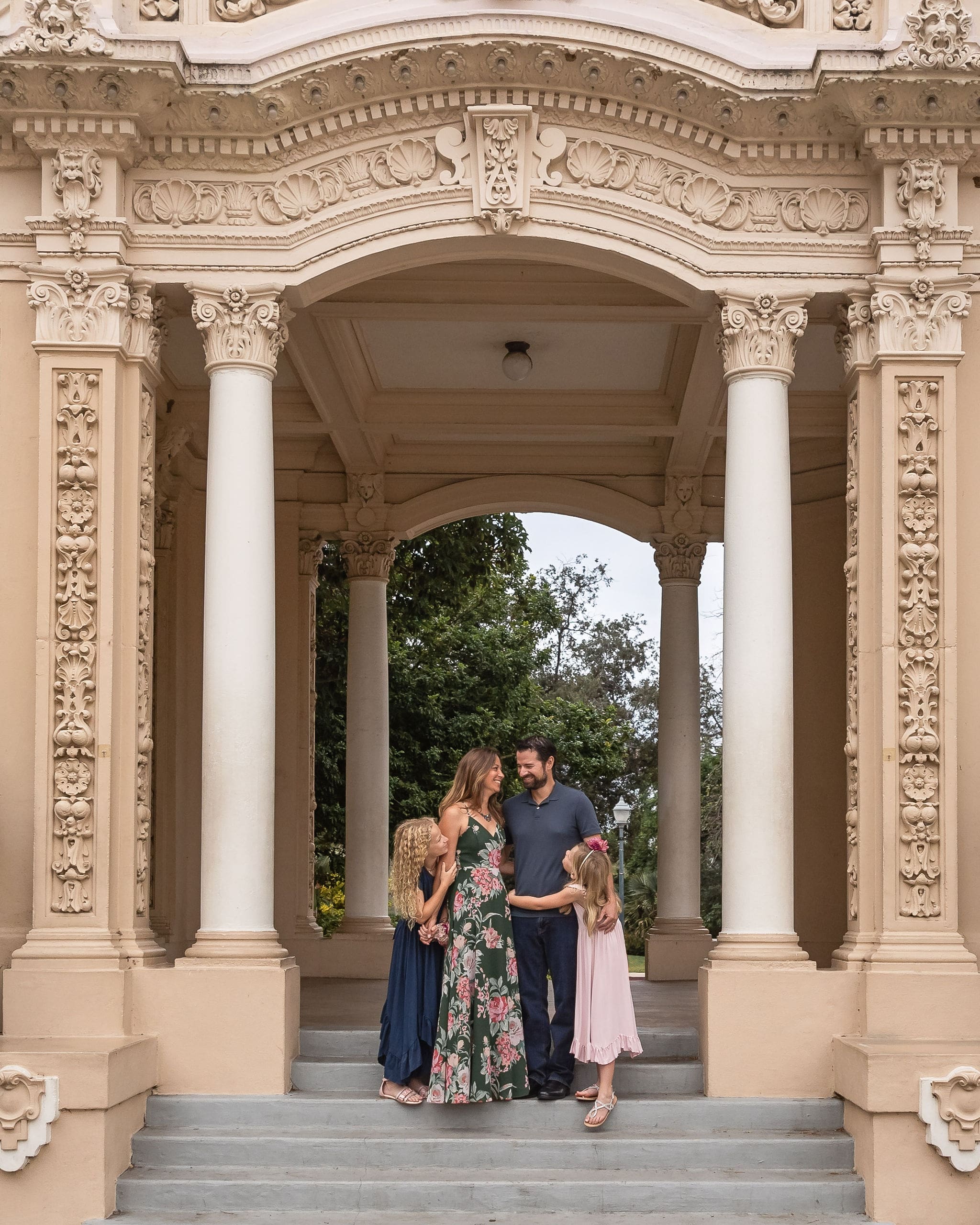 A happy mom and dad explore an ornate gazebo in a garden with their two young daughters after visiting pediatricians in san diego