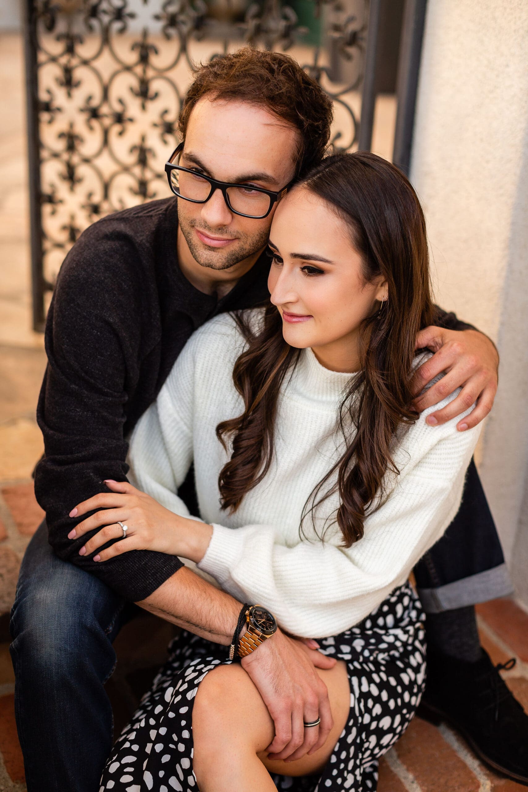 A happy engaged couple sits on steps cuddling in black and white outfits