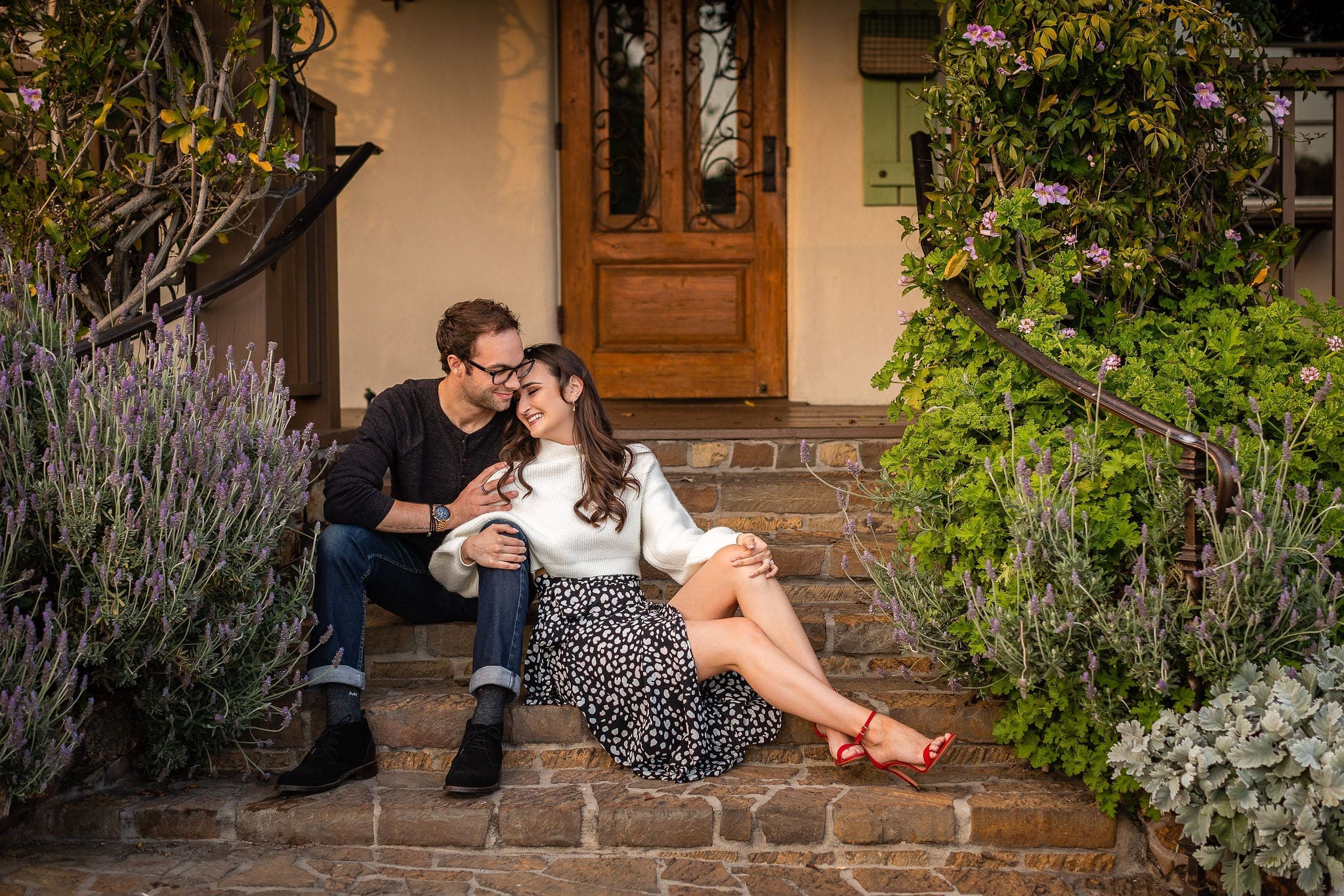 A happy woman in a white sweater sits on front steps leaning into her fiancee after enjoying romantic hotels in san diego